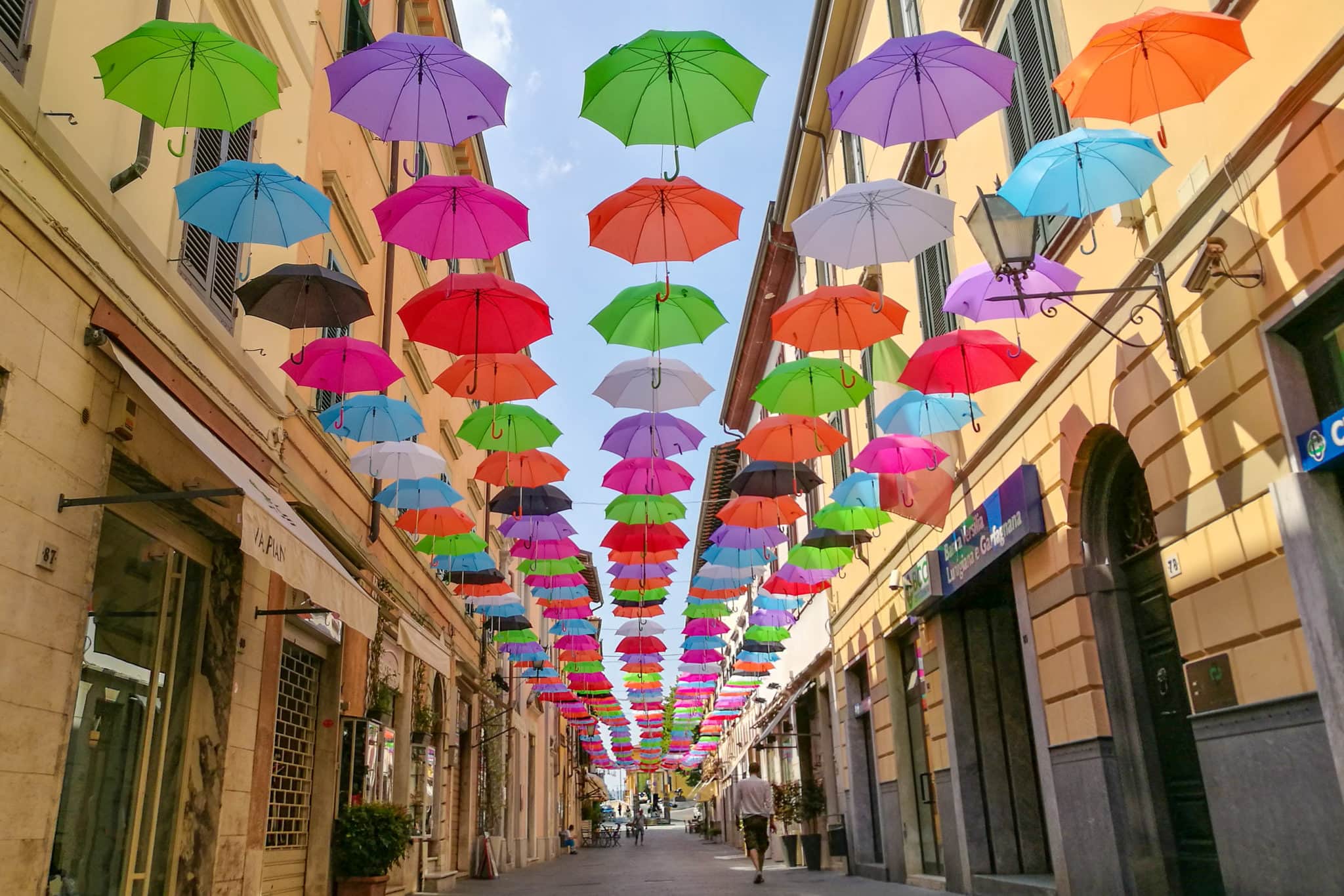 a person walking in Via Mazzini under the floating umbrellas in Pietrasanta
